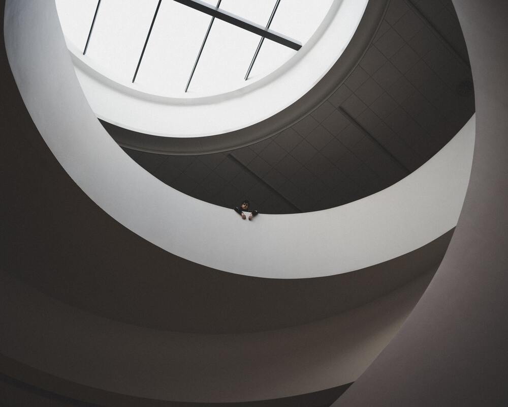 De grafische zwart-wit foto toont op afstand hoofd en armen, leunend over een balustrad, als was iemand verdwaald in een landschap van cirkels als in het Getty museum New York. Het beeld vormt een commentaar op dit blog over anti-cyclisch investeren.