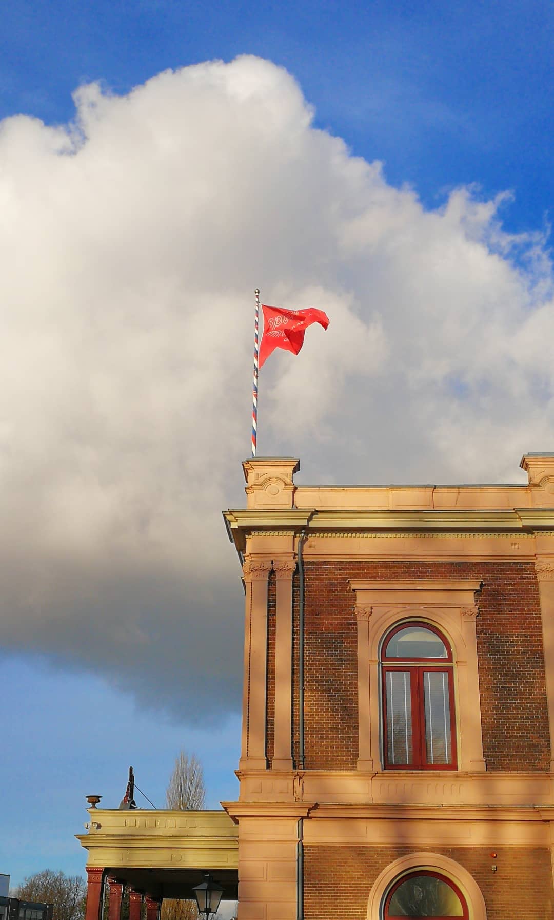De foto toont een uitsnede van een klassiek gebouw met een wapperende vlag. Welk verhaal vertelt dit beeld?